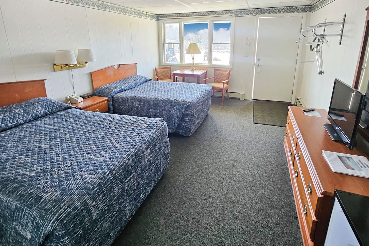A hotel room with two beds, a desk, a chair, a TV, and a window with a view.