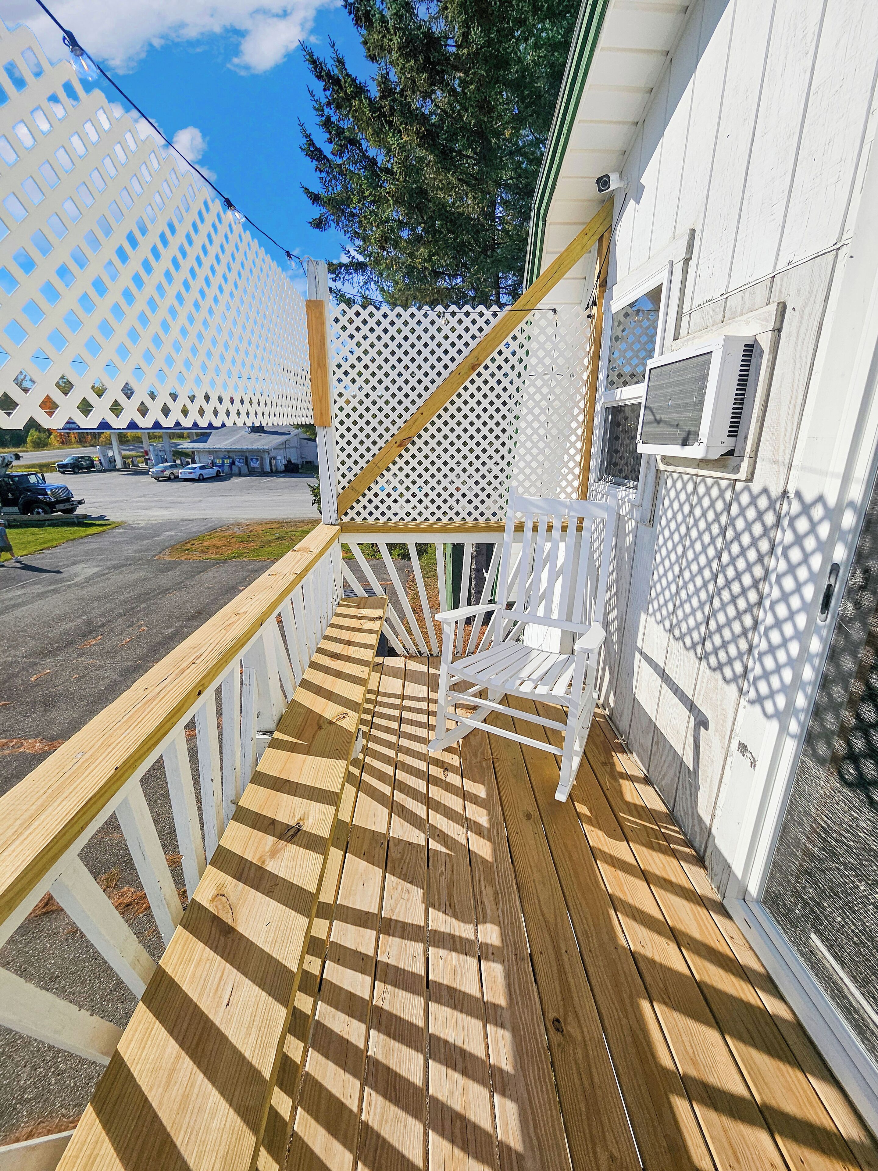 Eine Holzterrasse mit weißem Zaun, einem weißen Stuhl und einer Klimaanlage.