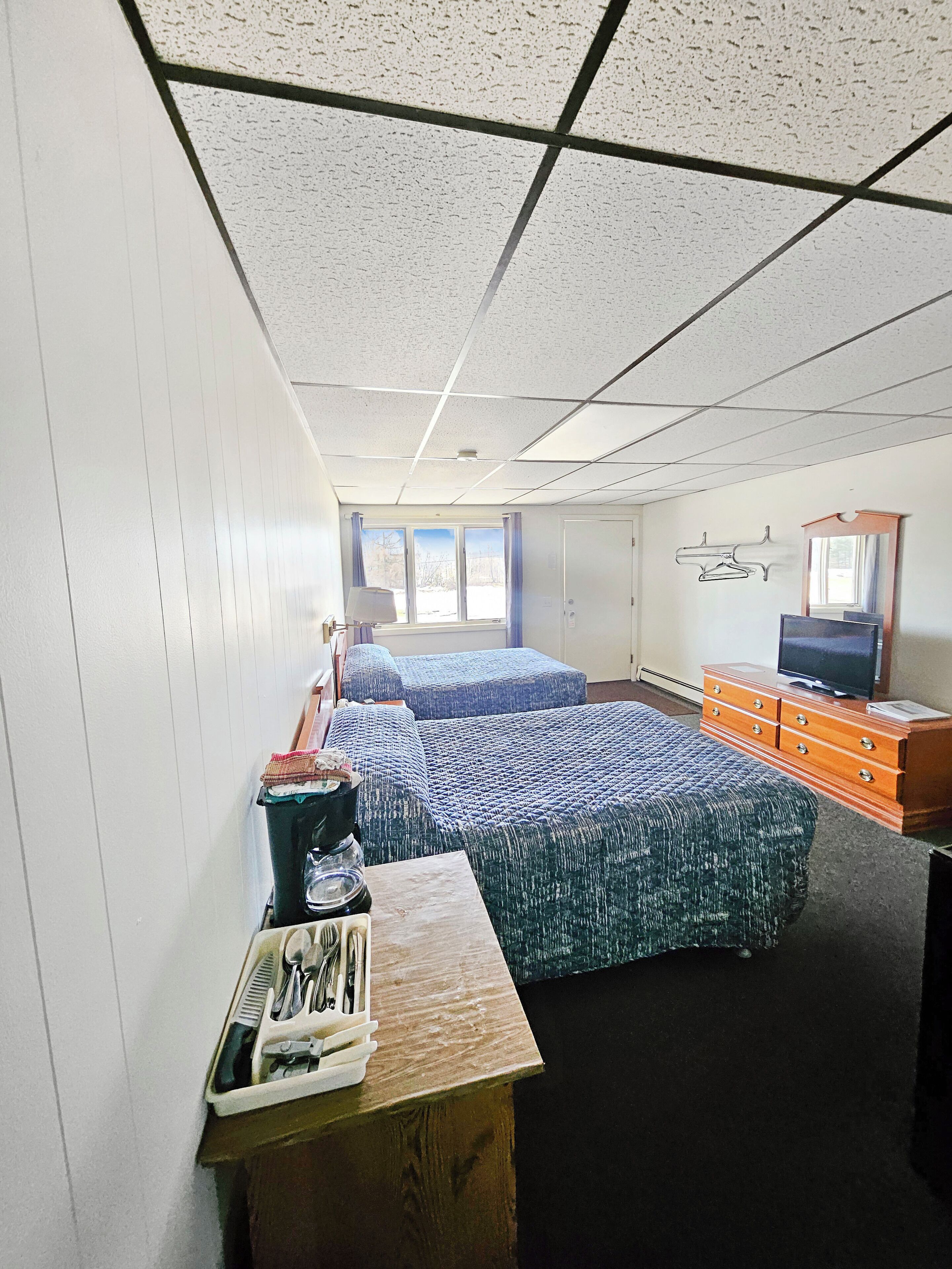 Un dormitorio con dos camas, un aparador, un televisor y una ventana con cortinas.