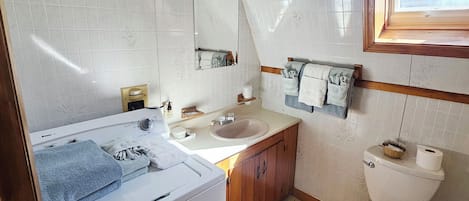 A compact bathroom with a washing machine, a sink, a toilet, and a window with a view of the sky.