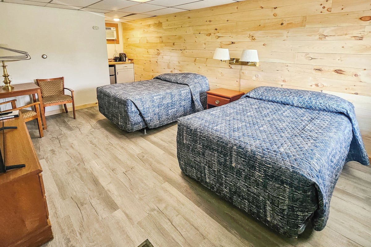 A room with two beds, a desk, a chair, and a wooden wall.