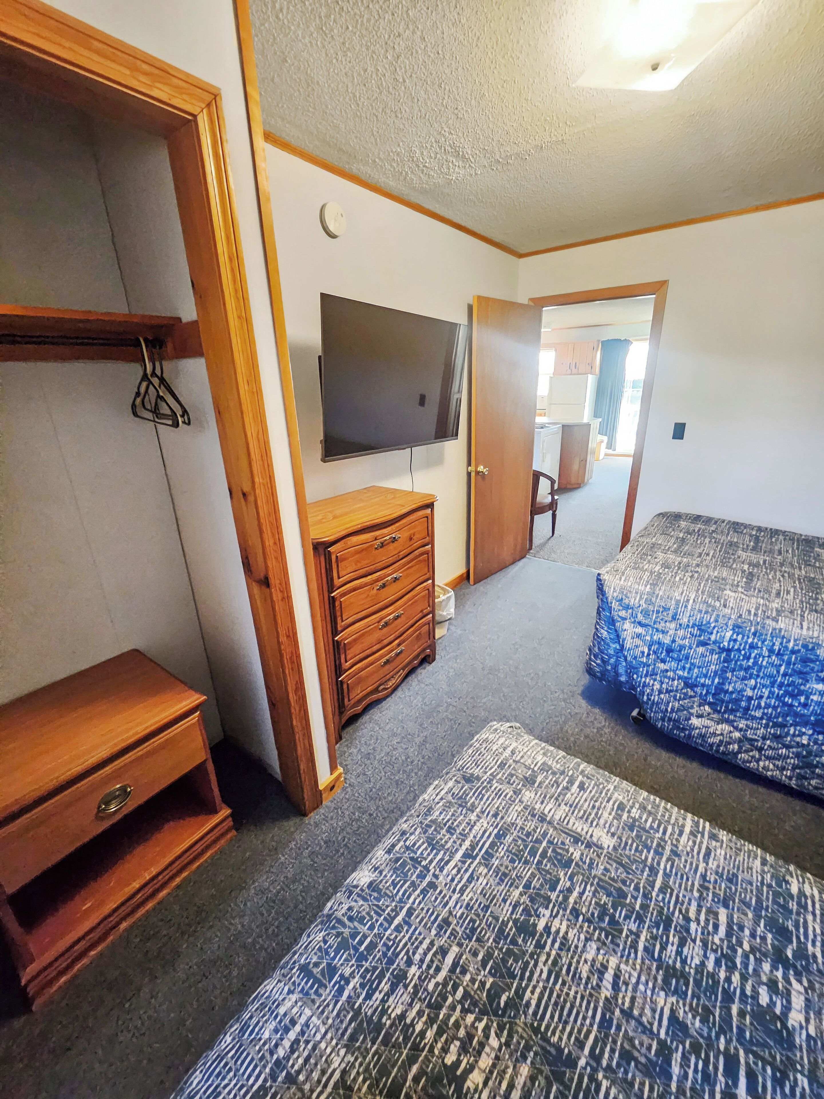 A room with a bed, a dresser, a TV mounted on the wall, and a door leading to another room.