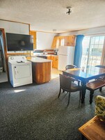 Cocina compacta con armarios de madera, estufa integrada, refrigerador y un amplio ventanal con cortinas.