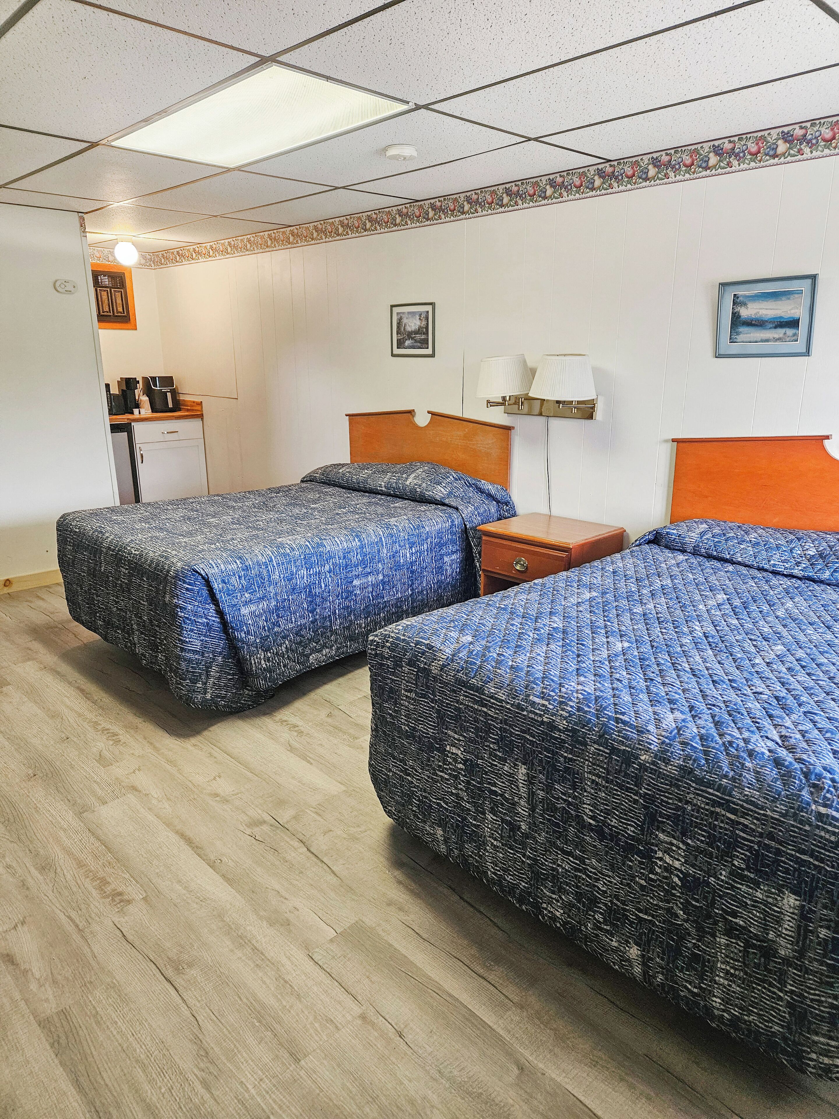 A room with two beds, a desk, and a small kitchenette.