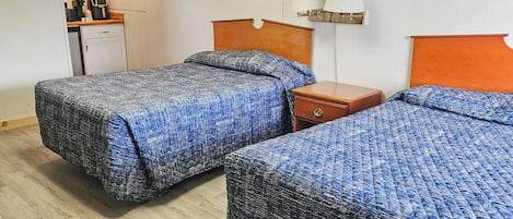 A room with two beds, a desk, and a small kitchenette.