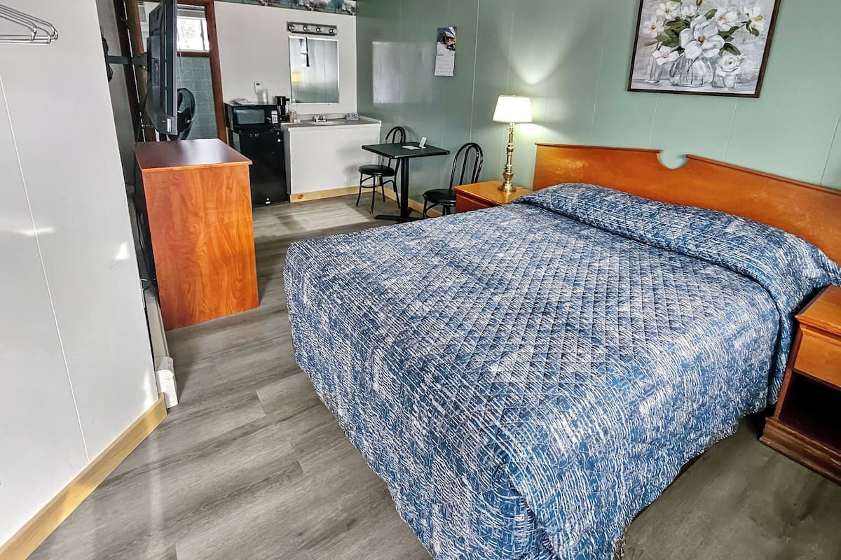 A hotel room with a bed, desk, chair, and a kitchenette area.
