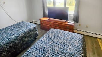 A room with two beds, a dresser, a television, and a window with curtains.
