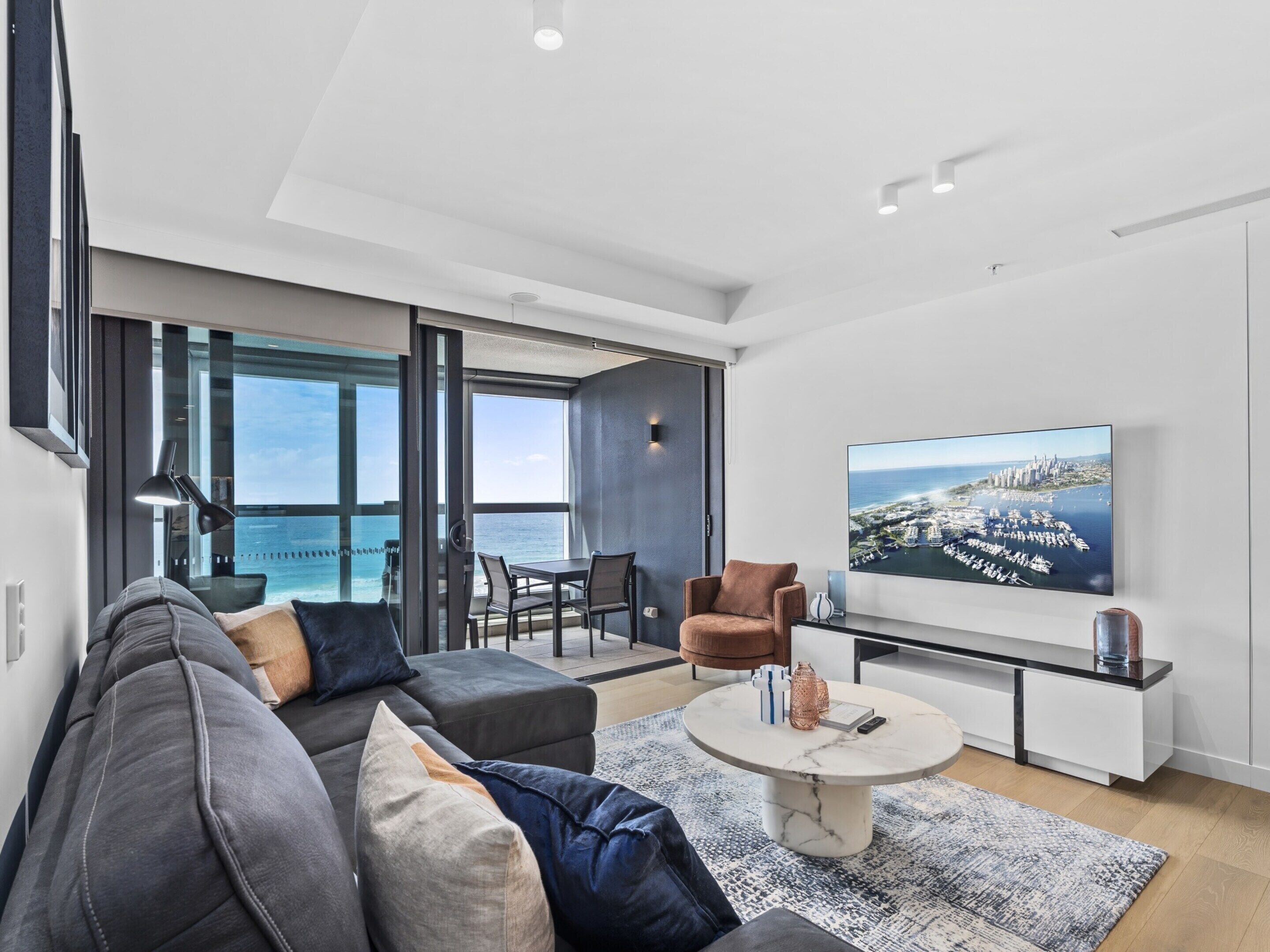 Een moderne woonkamer met een grote televisie, comfortabele zithoek en uitzicht op de oceaan.