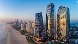 A coastal cityscape with modern skyscrapers, a beach, and a resort area with pools. - Luxury Beachfront 1-bed Apartment With Pool & Gym (Gold Coast)