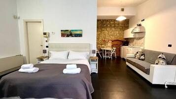 A hotel room with a bed, a sofa, a dining area, and a kitchen.