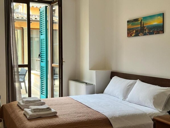 A hotel room with a bed, a painting on the wall, and a view through an open door.