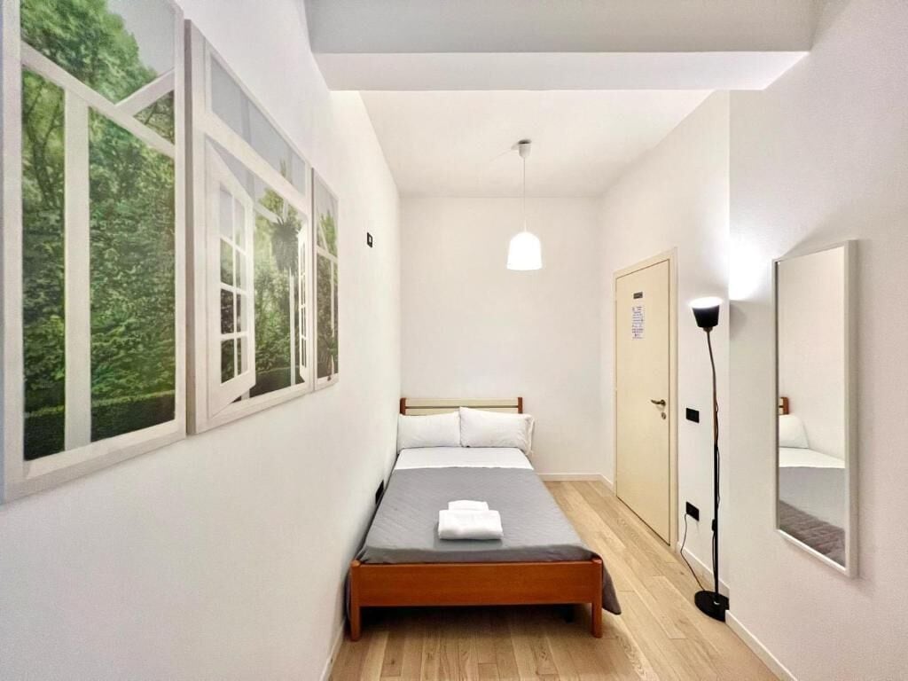 A bedroom with a bed, a wardrobe, a mirror, and a window with a view of greenery.