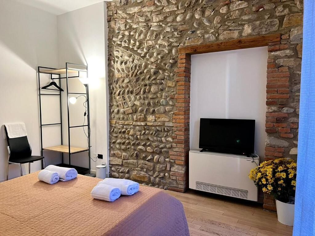 Une chambre d’hôtel avec un mur en pierre, un téléviseur à écran plat, un lit avec des serviettes, une chaise et une plante.