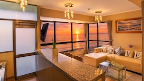 A modern living room with a large window, a sofa with 'LOVE' pillows, a glass coffee table, and a plant on the windowsill. - "Oceanfront 3BR, Home Office, Pool, Gym, Sauna, BBQ, Play area and Free Parking" (San Miguel)