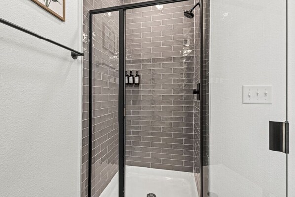A shower with a glass door, a tiled wall, and a white bathtub.