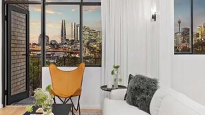 Ein modernes Wohnzimmer mit Stadtblick, einer Couch, einem Sessel und einem kleinen Tisch mit einer Pflanze.