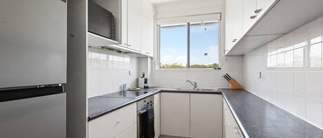 A modern kitchen with white cabinets, a black countertop, and a window providing natural light.