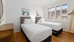 Habitación de hotel con dos camas, suelo de madera, ventana con persianas y un cuadro en la pared.