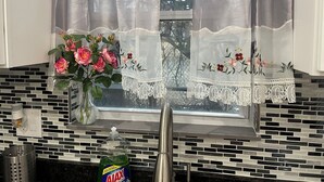 Una cucina con una finestra, un vaso con fiori e una bottiglia di detersivo Ajax Ultra.