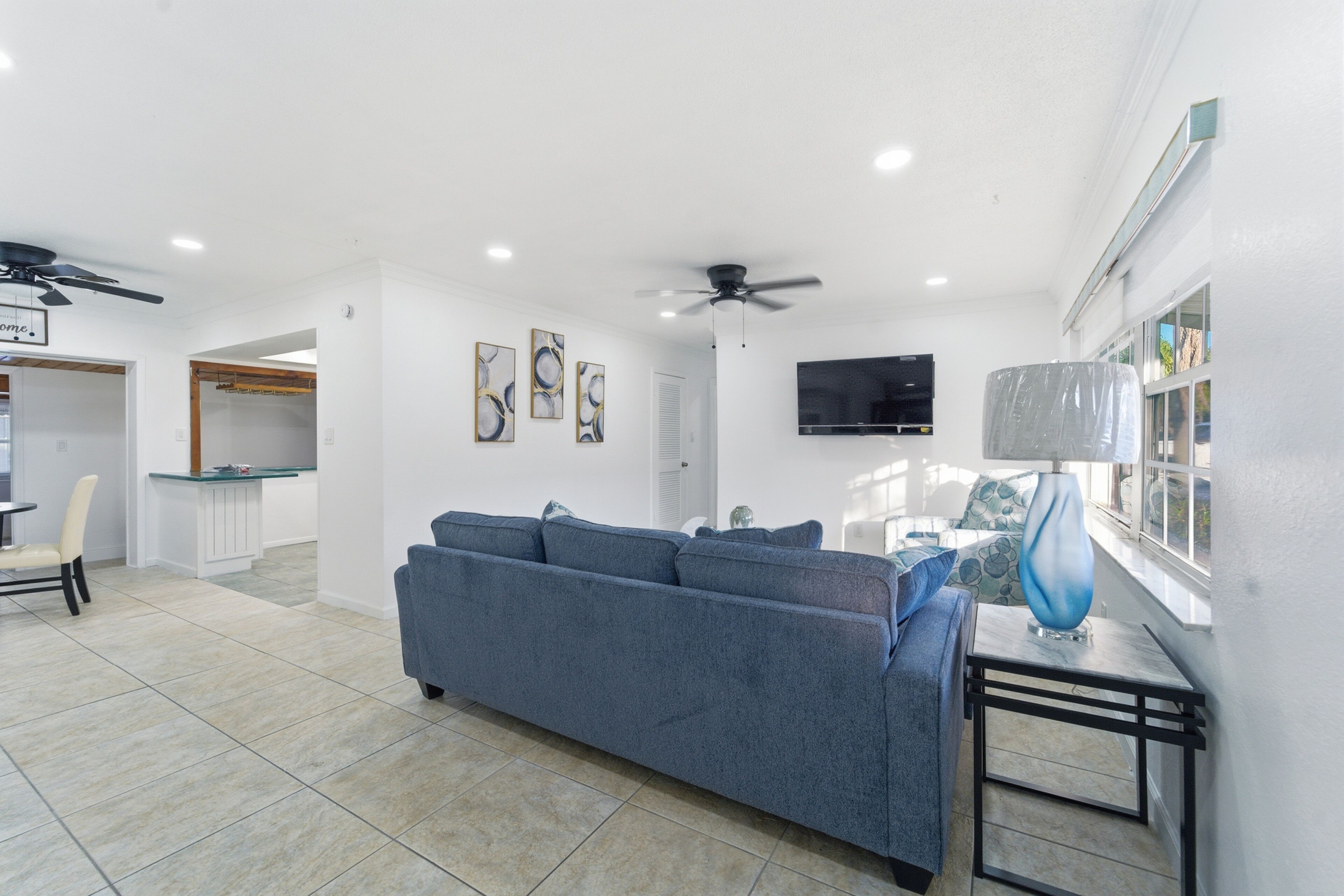 A living room with a blue sofa, a TV mounted on the wall, and a ceiling fan.