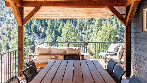 A wooden deck with a table and chairs, a sofa with cushions, and a view of a forested mountain. - Breathtaking View 12 Min to Downtown (Durango)