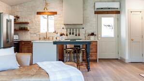 A modern kitchen with a stone wall, wooden cabinets, a central island with stools, and a hanging light fixture. - Breathtaking View 12 Min to Downtown (Durango)