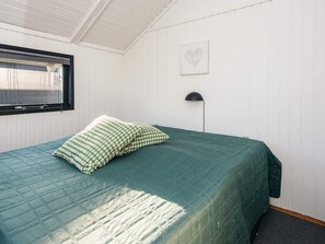 En enkeltseng med et grønt tæppe og mønstrede puder i et rum med hvide panelvægge og et skråt loft.