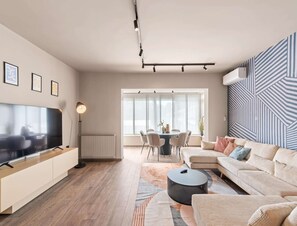 En moderne stue med et fladskærms-TV, et spiseområde med bord og stole, og en væg med mønster.