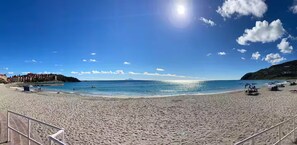 Ein weiter Sandstrand mit klarem, blauem Wasser, einigen Booten und einem entfernten Berg.