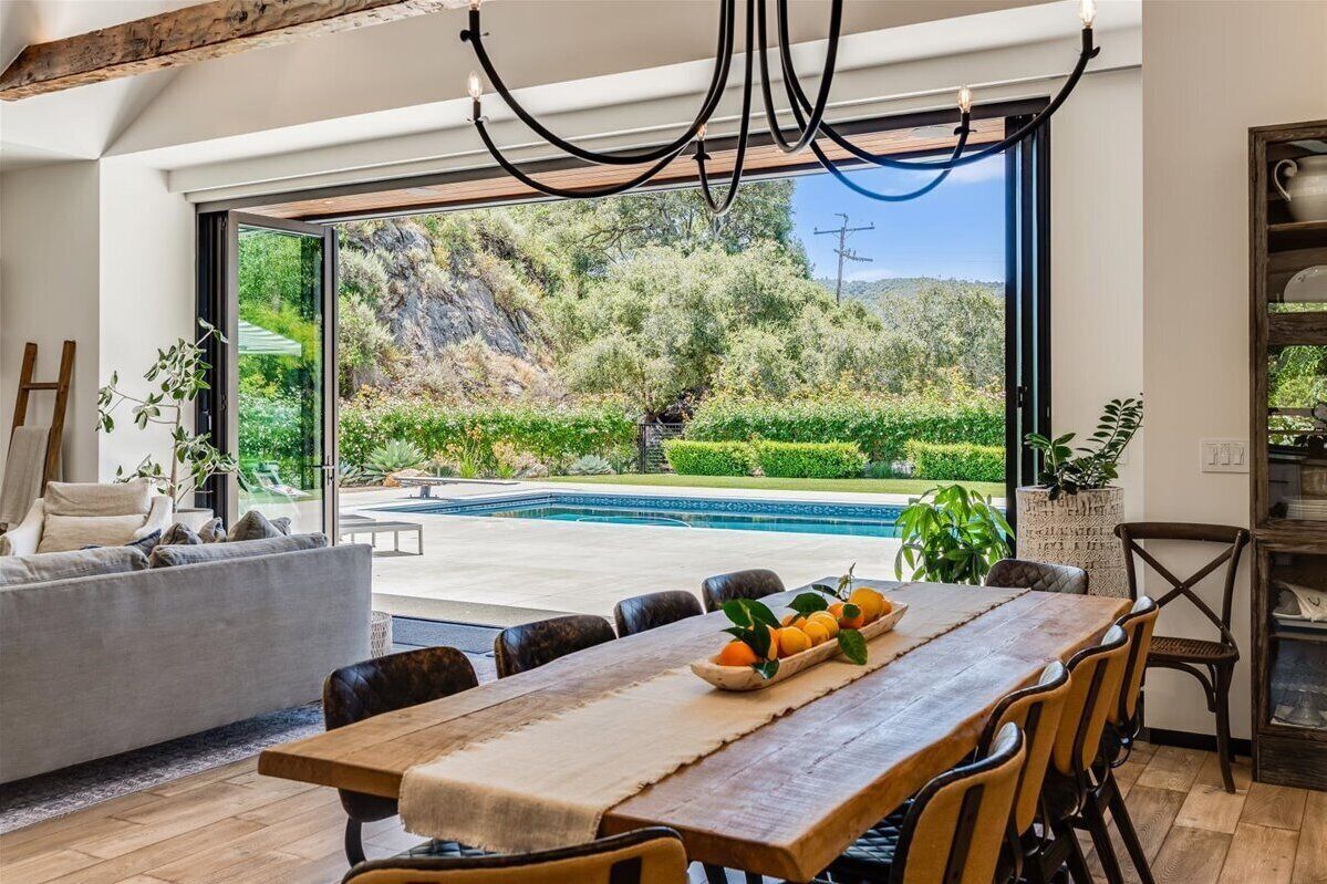 A modern interior with a dining area, a sofa, and a view of a pool and greenery.