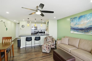 A modern living room with a sofa, a dining table, a kitchen in the background, and a ceiling fan. - Superior Oceanfront Condo Sugar Beach Resort Maui (Kihei)