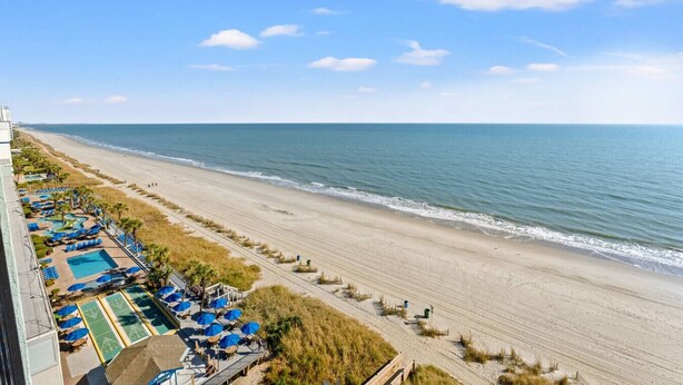 A beach resort with a long stretch of sandy beach, a pool area with umbrellas, and a clear view of the ocean. - Beachfront End Unit Condo with Pools and Hot tubs (Myrtle Beach)