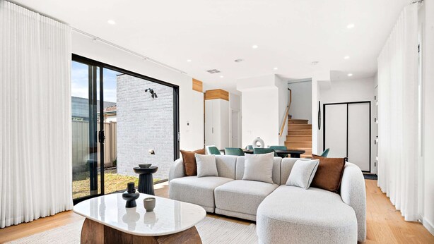 A modern living room with a sectional sofa, a coffee table, and a staircase leading to an upper level. - Brand-new 3-bed Townhouse in Pascoe Vale (Melbourne)