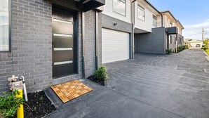 A modern residential building with a garage, a small garden area, and a paved driveway. - Brand-new 3-bed Townhouse in Pascoe Vale (Melbourne)