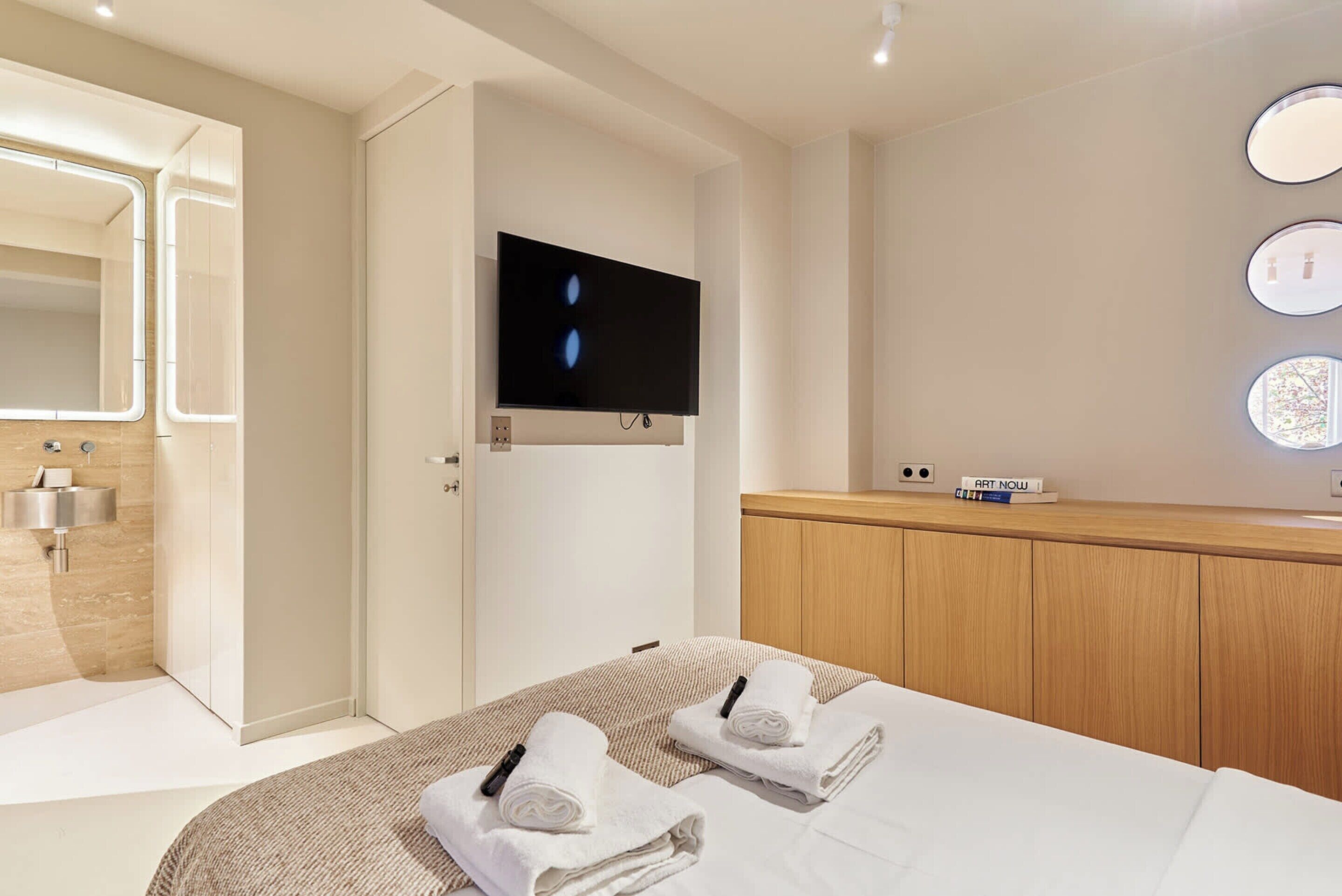 Une chambre d’hôtel moderne équipée d’un lit, d’une télévision, d’un miroir, d’un lavabo et d’une armoire en bois.