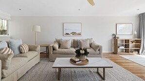 Ein Wohnzimmer mit einem beigefarbenen Sofa, einem Couchtisch mit Dekoration, einem Holzregal und einem Deckenventilator.