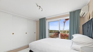 Ein Schlafzimmer mit Bett, einem fensterbehangenen Fenster, einer Klimaanlage und Blick ins Grüne.