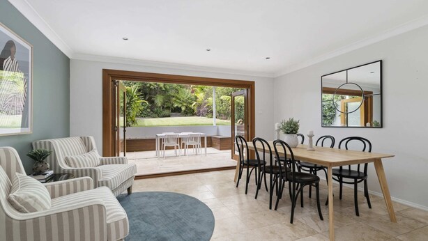 Ein geräumiger Wohnbereich mit Esstisch und Stühlen, einer Couch und einem großen Fenster mit Blick auf einen Garten.