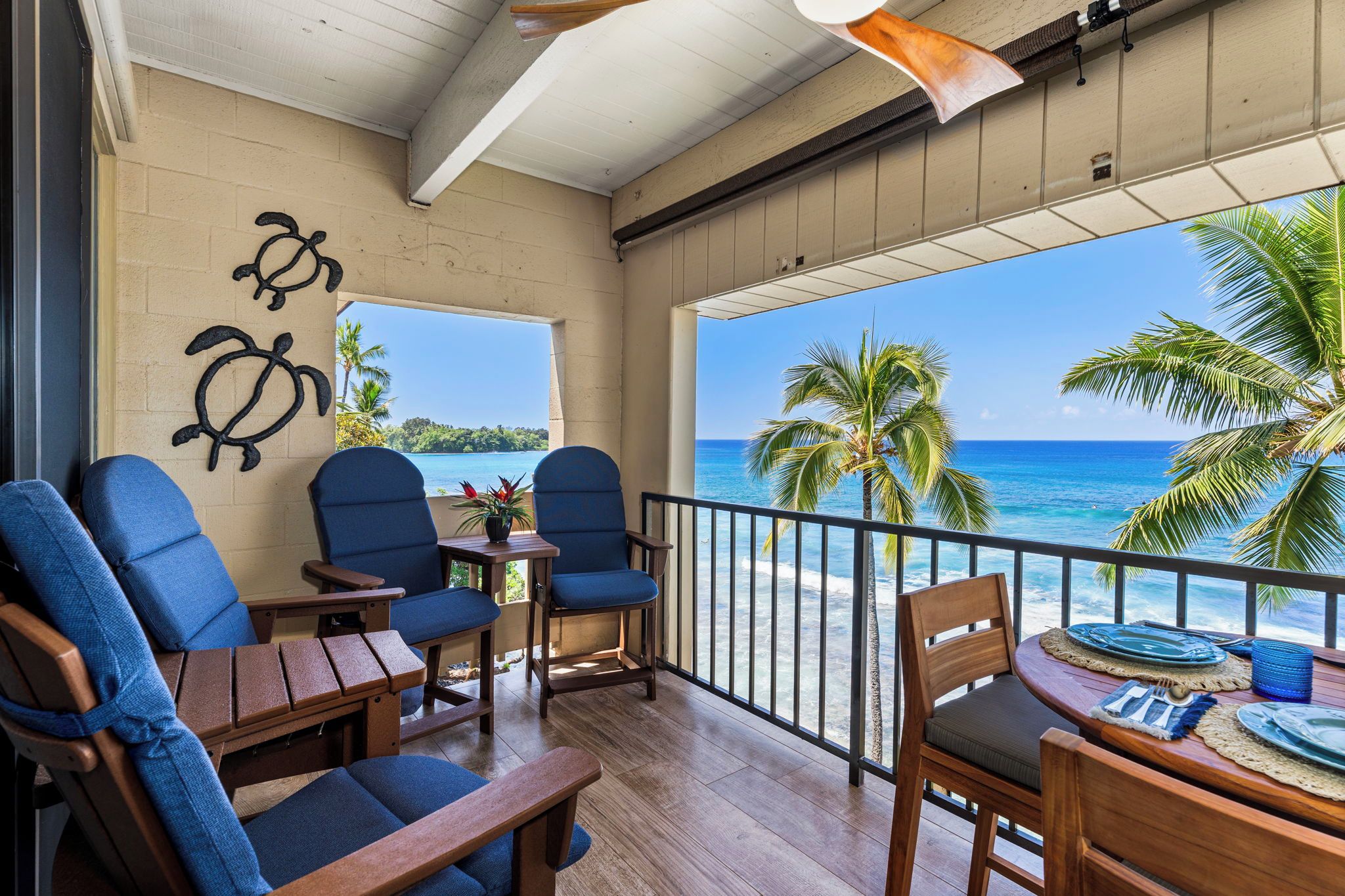 A balcony with wooden furniture, a view of the ocean, and a palm tree.