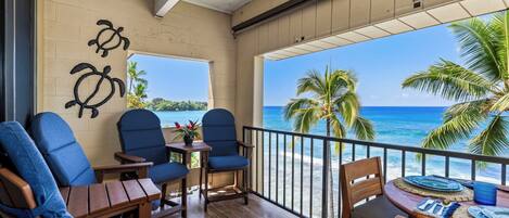 A balcony with wooden furniture, a view of the ocean, and a palm tree.