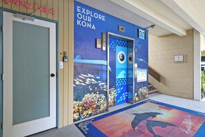 Entrada de hotel com uma placa que diz 'Explore Our Kona' e um mural colorido com vida marinha.