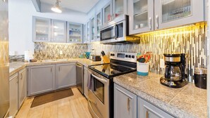 Una cocina moderna con electrodomésticos de acero inoxidable, encimera de granito y una lámpara colgante de diseño vertical.