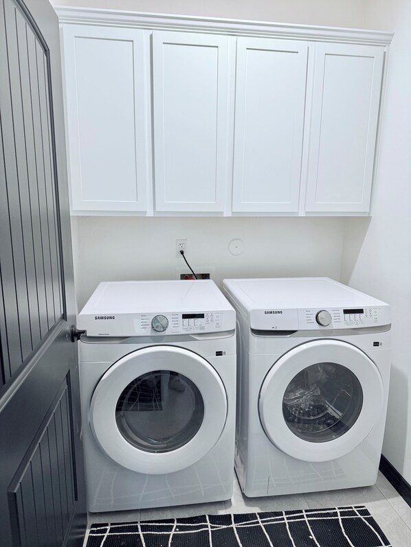 Two white Samsung front-loading washing machines in a laundry room with white cabinets above. - Experience luxury at "A&B Oasis in the Desert," an exceptional 3-bed, 2-bath (Carlsbad)