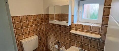 A bathroom with a toilet, sink, mirror, and a window above the mirror.