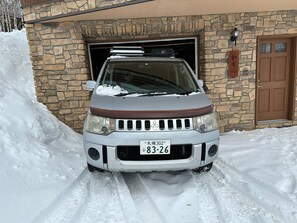 A vehicle parked in front of a stone building with a garage door, snow on the ground, and a wooden door to the right. - LUXURY SKI OR GOLF HOME 
4 Bedroom, 3.5 Bathroom 
Walk to Rusutsu Resort, Japan (Rusutsu, Abuta-Gun)
