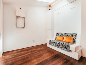 A room with a wooden floor, a white sofa with a floral cover, and a white wardrobe. - Modern & Historic Apartment in Lisbon (Lisbon)