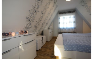 Un dormitorio con cama, cómoda, mesita de noche y ventana con cortinas.