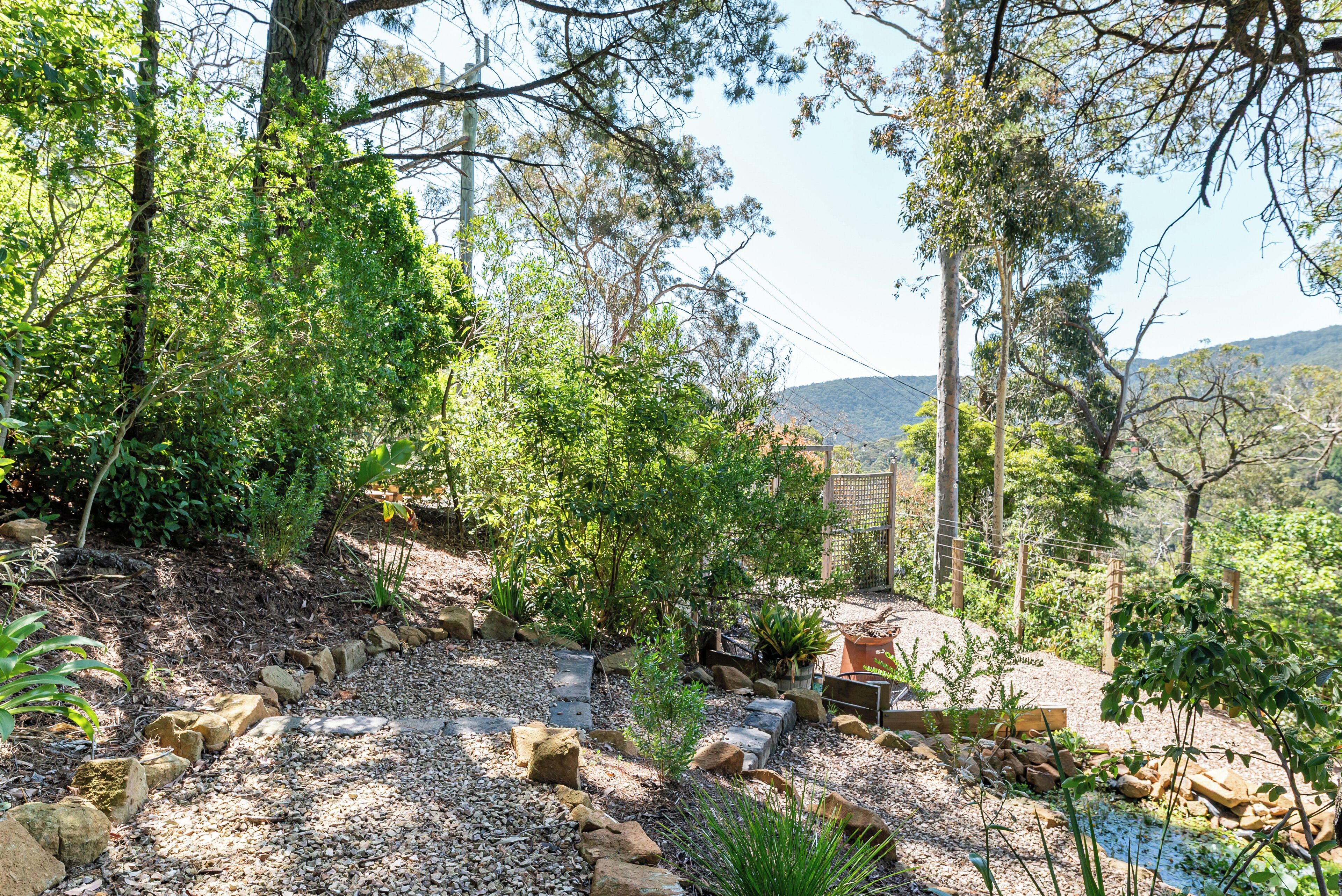 Un jardin agrémenté de diverses plantes et de rochers, d’un banc en bois et d’un petit étang.
