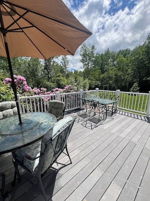Une terrasse dotée de mobilier d’extérieur, d’une table avec un plateau en verre et d’un grand parasol.