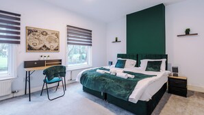 A modern bedroom with a large bed, a desk, and a chair. There are two windows with blinds, a map on the wall, and a green accent wall. - Walkden, Worsley 4 Bedroom House w/ Free Parking (Worsley)